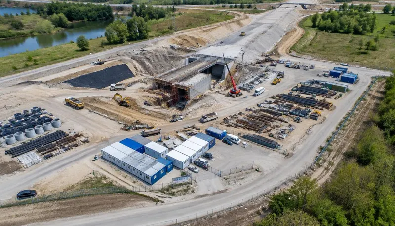 Vista aérea de obra de infraestrutura com acessos, máquinas, pátio de materiais e canteiro administrativo